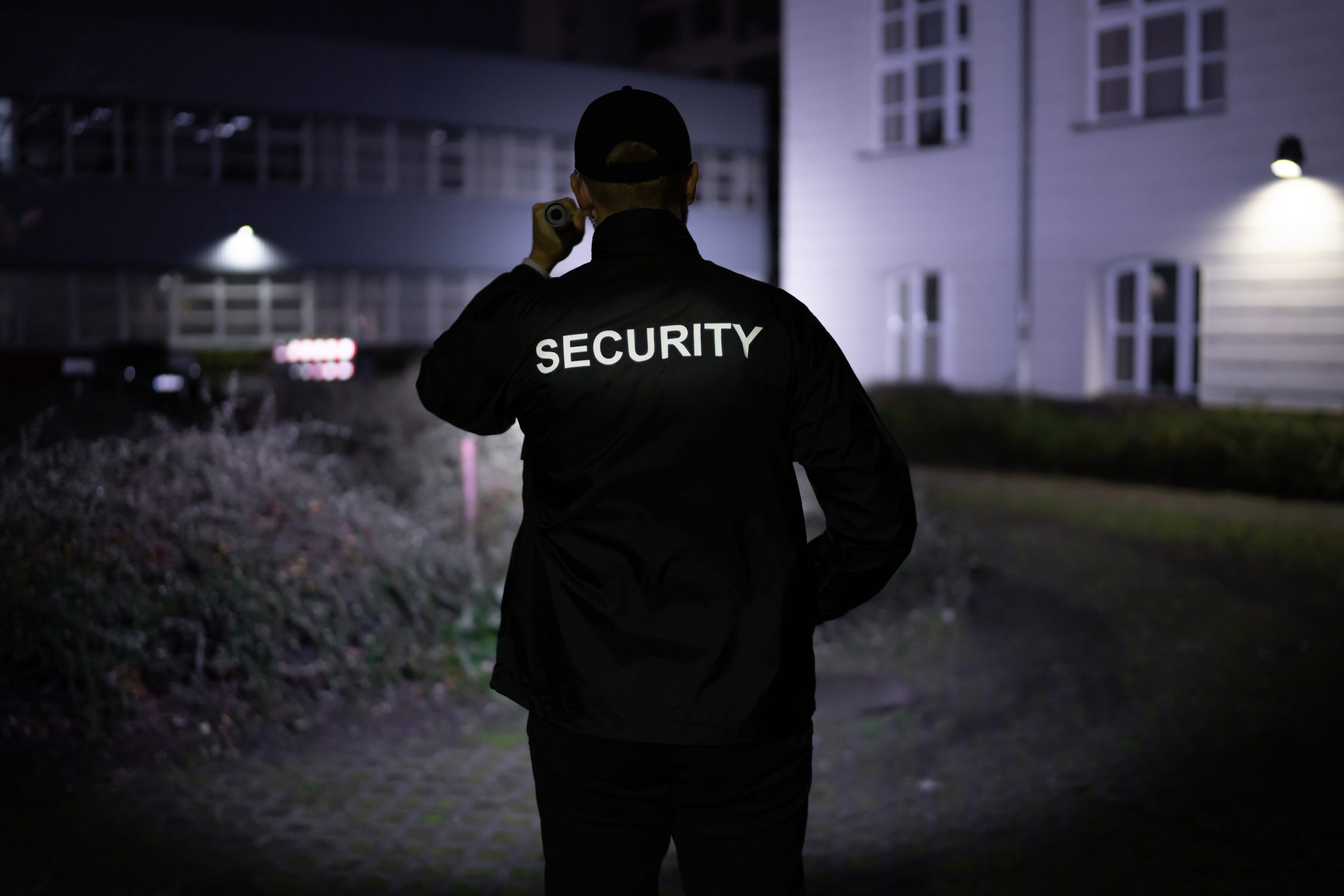 A security worker in a black jacket patrolling a commercial building at night