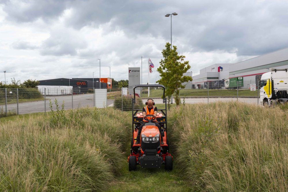 A sit on lawn mower cutting the grass on a large factory site.