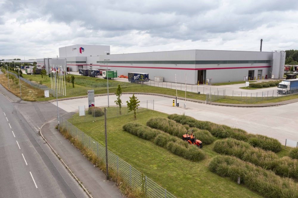 A sit on lawn mower cutting the grass on a large factory site.
