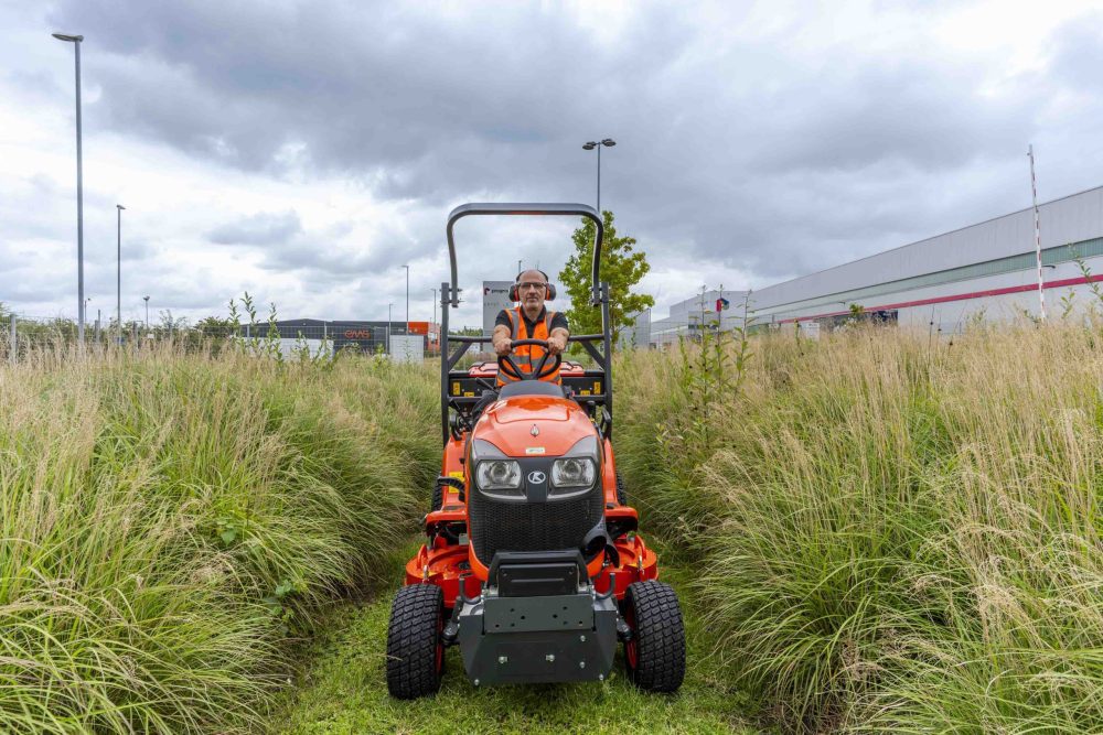 A professional grounds worker rides a sit on mower through the long grass on a client site.