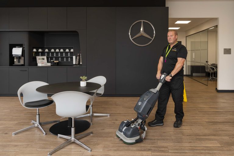 A professional cleaner using a polishing machine in an office communal area.