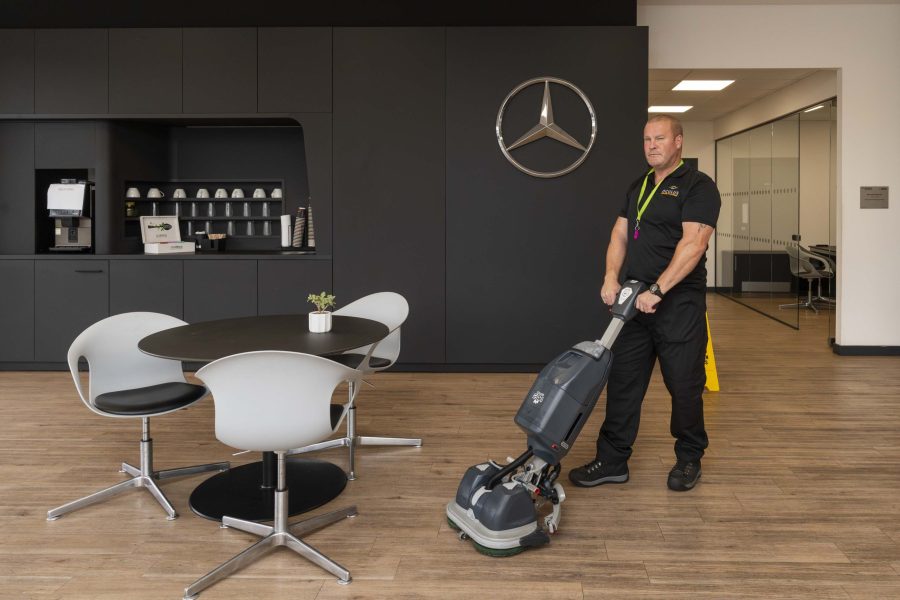 A professional cleaner using a polishing machine in an office communal area.