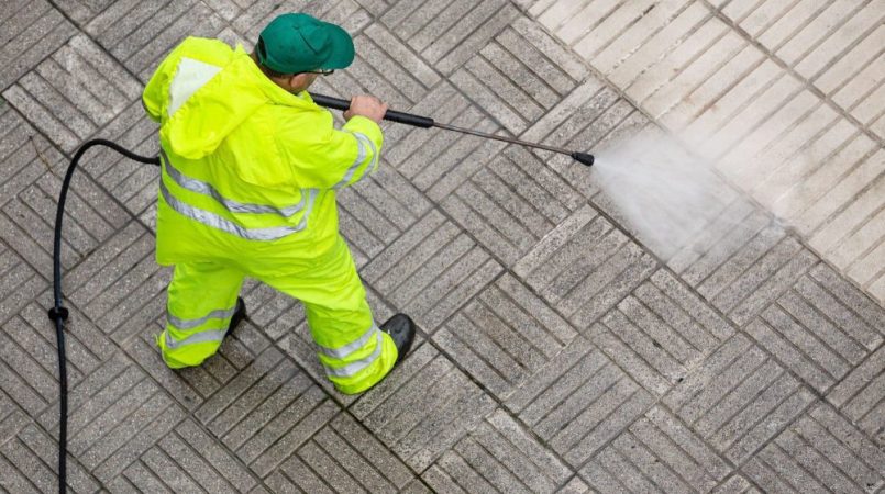 A man power washes a patio, in protective clothing.
