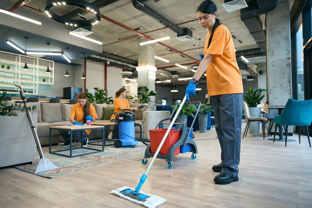 A professional cleaner mopping a wooden floor in a communal office area.